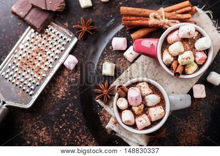 Hot chocolate with marshmallows and spices on grunge dark table. Selective focus, tasty holidays concept. Drink for fall and winter. Top view overhead flat lay