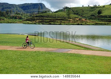 NUWARA ELIYA SRI LANKA - OCTOBER 18 : The girl rides her bicycle near lake in Nuwara Eliya. October 18 2011 in Nuwara Eliya Sri Lanka.