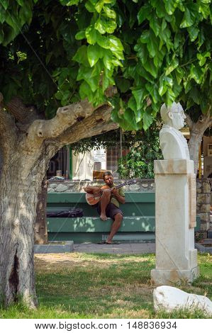 SITIA, CRETE, GREECE - 2016: Street musician is playing guitar on bench in park of Sitia town on Crete island, Greece.
