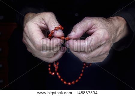 Close view of men's hands with rosary on a dark background