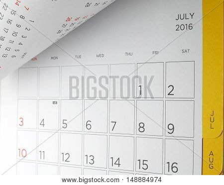 close up cardboard desk calendar with days and dates of July 2016 in grid and yellow edge, acronym letters US in fourth of July, symbol of American Independence Day, flip the calendar page