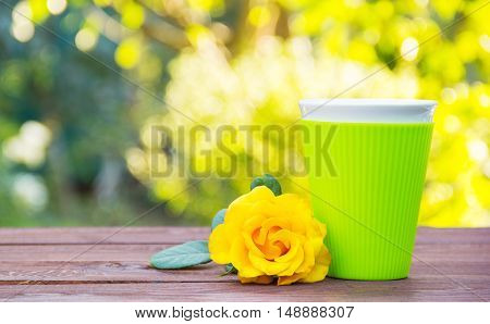 A glass of green color with a fragrant hot tea. Yellow rose and tea on a wooden table. Romantic concept. Natural green background. Green blur. Copy space.