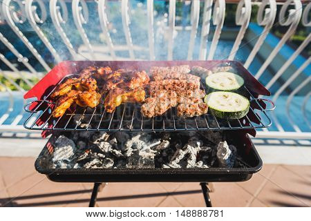 Delicious meat on barbecue grill with coal on balcony. Grilling food on a balcony or a terrace with wonderful view. Small cheap BBQ grill at home.