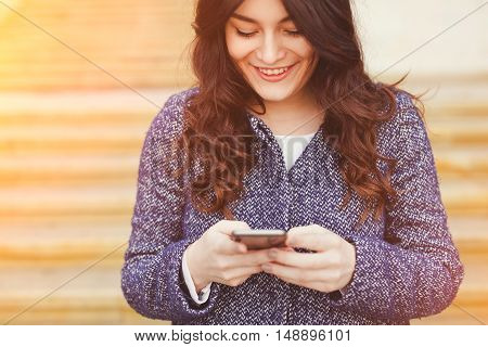 Closeup caucasian woman female using cellphone smartphone walking while texting. Brunette girl wearing a coat smiling and using map app to navigate on city streets