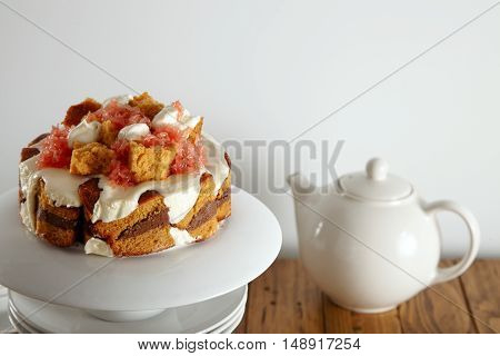 Close up shot of a delicate light brown cake with cream, grapefruit and chocolate filling on a pyramid of white teaware next to a teapot