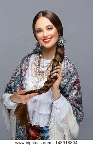 Happy beautiful young russian woman with very long braid in traditional shawl. Red lips. Over grey background.