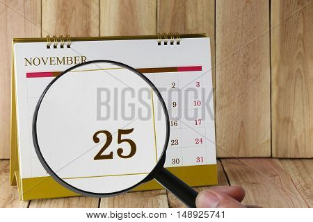 Magnifying glass in hand on calendar you can look Twenty Five days of monthFocus number Twenty Five in NovemberConcept in business and meetings.
