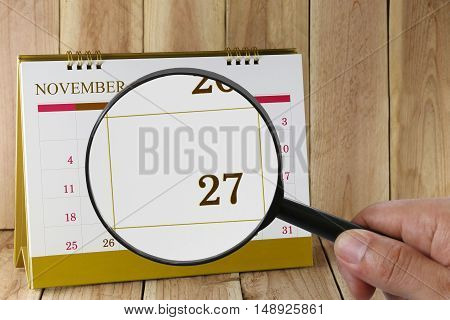Magnifying glass in hand on calendar you can look Twenty seven day of monthFocus number Twenty seven in NovemberConcept in business and meetings.