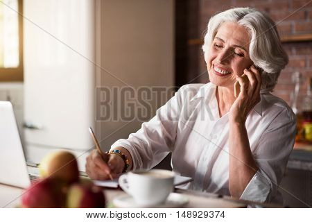 Smiley. Pleasant old lady communicating with her family and friends using telephone and laptop