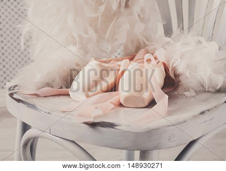 Pastel pink ballet shoes background. New pointe shoes with satin ribbon lay on white rustic shubby chic chair near feather boa