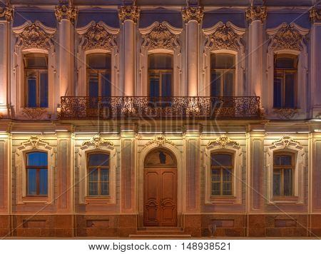 Several windows in a row balcony and door on night illuminated facade of urban apartment building front view St. Petersburg Russia