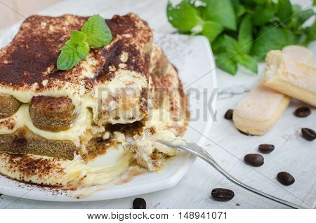 Tiramisu, traditional Italian creme dessert with mint leaves and coffee beans on white wooden background. Tiramisu cake. Homemade tiramisu dessert close-up. Italian cuisine concept. Selective focus.
