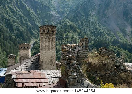 Poor people houses are nested near old stone towers. Covered with forest mountain in background.