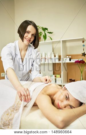 Beautician covers body of woman on procedure in beauty salon.