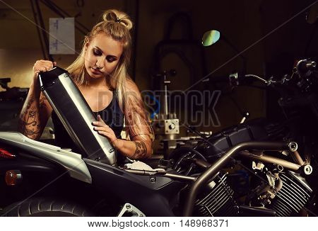 Blond woman mechanic holding a muffler in a motorcycle workshop