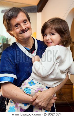 A Man With Downs Syndrome Carrying His Great Niece.  They Are Both Happy And Looking At The Camera. 