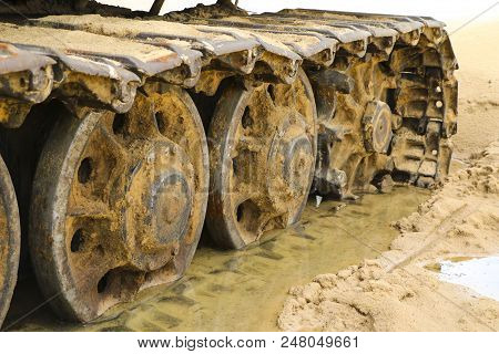 Old Iron Caterpillar In Wet Sand. Rusty Steel Wheels And Caterpillar Tape Of A Large  Bulldozer, Tan