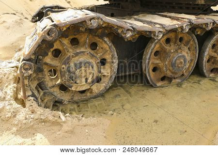 Old Iron Caterpillar In Wet Sand. Rusty Steel Wheels And Caterpillar Tape Of A Large  Bulldozer, Tan