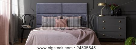 Pastel Pink Bedclothes On King-size Bed With Soft Bedhead Standing In Dark Bedroom Interior With Gol