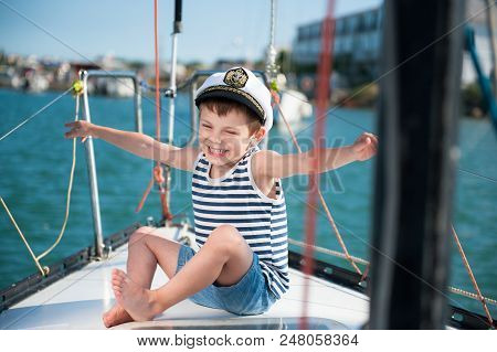 Happy Delightful Kid In Captain Cap Sitting On Luxury Yacht Board