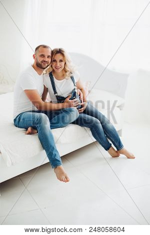 Beautiful And Stylish Couple Of Handsome Man And Pretty Blonde Pragnant Woman Sitting On Bad And Emb