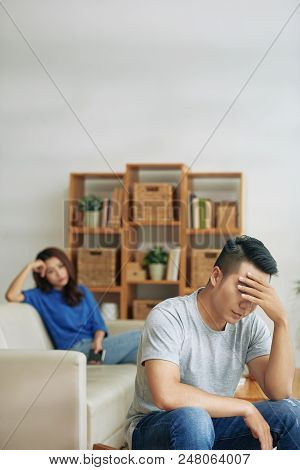 Upset Asian Man With Girlfriend On Background Sitting In Deep Sadness Having Miscommunication Proble