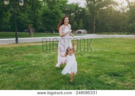 Laughing Woman In Light Dress Running Catching Up With Little Cute Child Baby Girl On Green Grass La