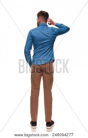 back view of relaxed casual man scratching his head and  loking to side while standing on white background, full length picture