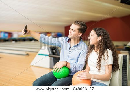 Smiling Teenage Couple With Bowling Balls Taking Selfportrait Using Smartphone In Club