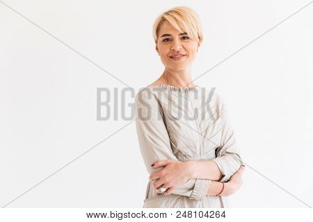 Portrait of cheerful mature blond woman 40s looking at camera with kind smile and arms folded isolated over white background in studio