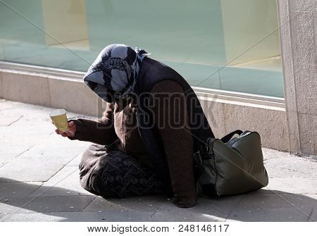 Elderly Gypsy Asks Alms Sitting On The Ground With A Glass
