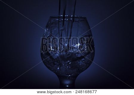 Simple Still-life Photo Of Whisky Glass, Water Jet And Dim Colour Light