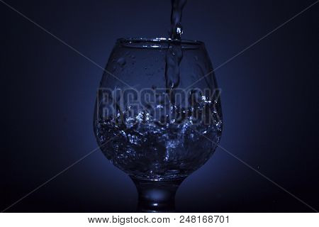 Simple Still-life Photo Of Whisky Glass, Water Jet And Dim Colour Light