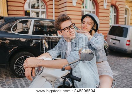 Tired Girl Is Sitting Behind Her Boyfriend On Motorcycle And Leaning To Him. She Is Looking At Him. 