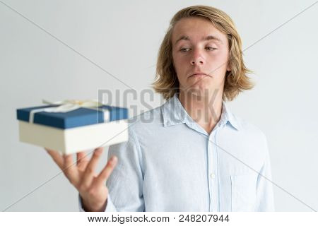 Confused Handsome Guy Disappointed With Gift Box Size. Long Haired Young Caucasian Man Looking At Pr