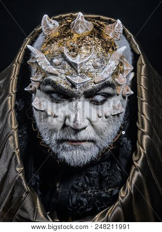 Man With Thorns Or Warts, Face Covered With Glitters. Demon With Golden Hood On Black Background. Se