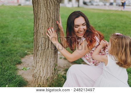 Laughing Woman In Light Dress Play And Have Fun With Little Cute Child Baby Girl On Green Grass Lawn