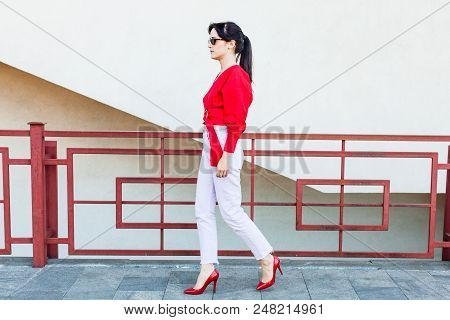 Young Stylish Woman In A Red Blouse And White Trousers Walking In The City Wearing Highheel Shoes