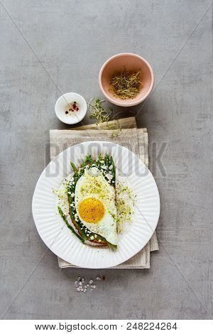 Fried Egg, Green Aspargus, Feta Cheese And Micro Greens Spring Sandwich On Plate Over Light Concrete