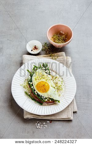 Spring Sandwich Of Green Aspargus, Fried Egg, Feta Cheese And Micro Greens On Plate Over Light Concr