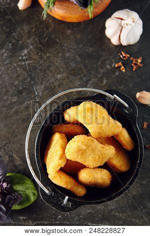Heap of Delicious Chicken Nuggets in Metal Bowler on Dark Background. Caloric Protein Product Surrounded by Spices. Chicken Fillet in Breading
