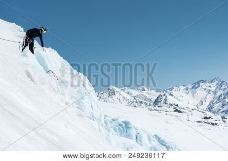 A Professional Mountaineer In A Helmet And Ski Mask On Insurance Makes A Nick-hole In The Glacier Ag