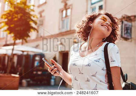 Beautiful Young Girl Using Smartphone And Listening To The Music Walking On Street. Happy Woman Danc
