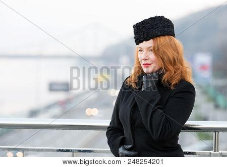 Business Lady Has Rest On Balcony. Aged Women Model In Black Coat And Gloves. Woman On Bridge Waitin