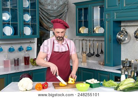 Serious Cook In Red Apron And Red Bonnet At Kitchen Cut Yellow Paprika For Two Parts On Cutting Boar