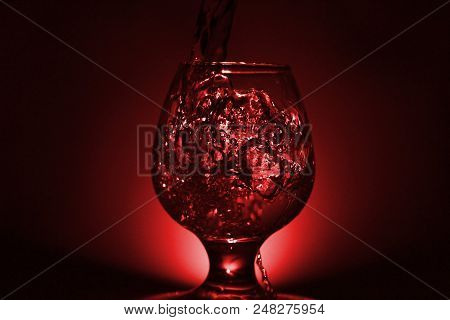 Simple Still-life Photo Of Whisky Glass, Water Jet And Dim Red Light