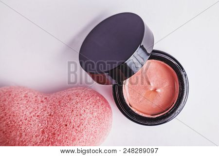 Cosmetic Set Of Pink Clay Face Mask And Light Pink Heart Shaped Konjac Sponge. Top View On White Bac