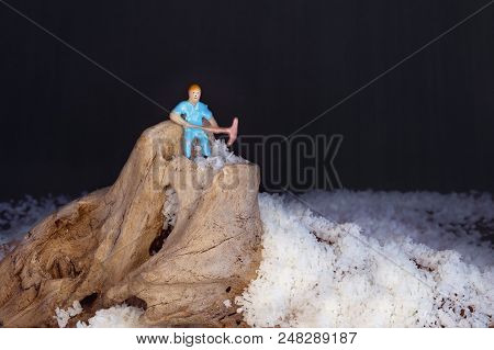 A Tiny Miniature Male Worker Figure With Pick Standing On Top Of A Timber Mountain Surrounded By Pil