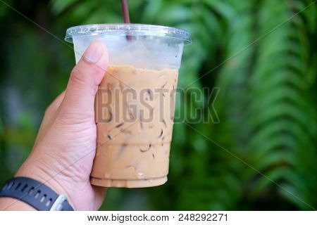 Hand Holding A Glass With Iced Coffee With Tree Background