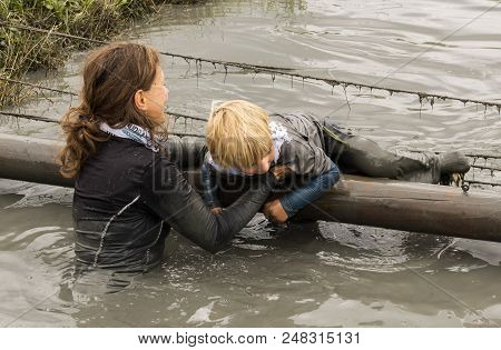 Biddinghuizen, The Netherlands - June 23, 2018: Woman Helping Child During A Mud Run (mudraise) In T